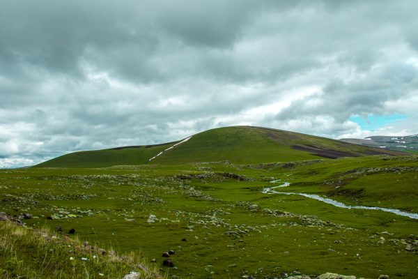 A beautiful landscape featuring rolling green hills and a stream under a cloudy sky. Nature 4K