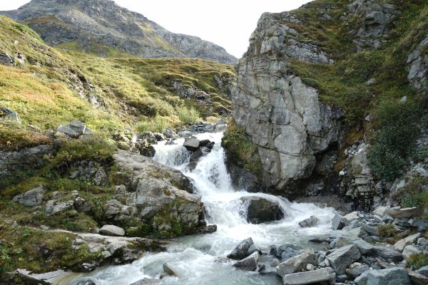 A beautiful mountain waterfall cascades through rugged rocky terrain, surrounded by lush greenery. Nature 4K