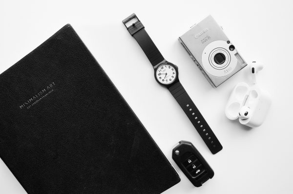 A black and white flat lay featuring a notebook, wristwatch, digital camera, earphones, and car key Minimaliste 4K