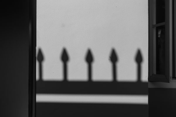 A black and white photo of fence shadows cast on a wall, creating a geometric pattern. Dark 4K
