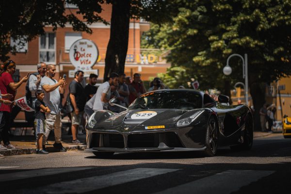 A black sports car driving through city streets during a public automotive event. Voitures 4K