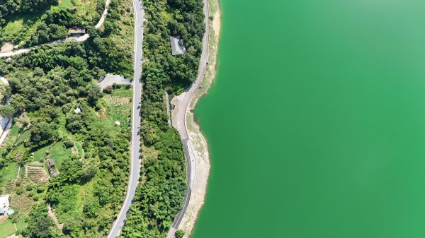 A breathtaking aerial view showcasing a winding road beside a lush green landscape and tranquil lake. Nature 4K