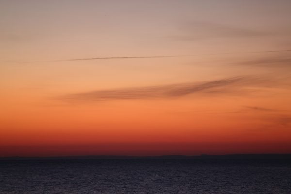 A breathtaking sunset view over a calm ocean horizon, showcasing vibrant orange hues and wispy clouds. Nature 4K