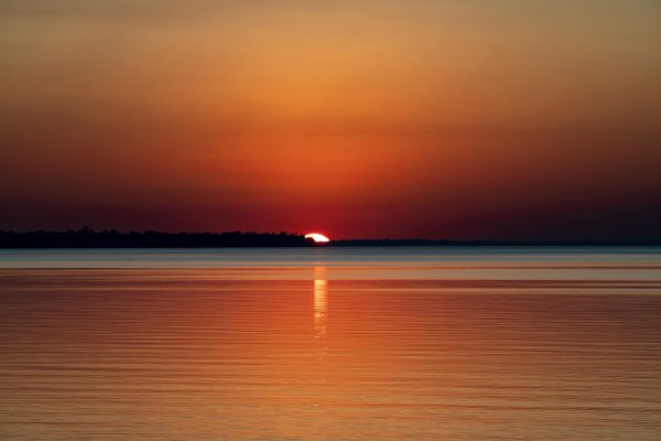 A breathtaking sunset with vibrant colors reflecting on a tranquil water surface. Nature 4K