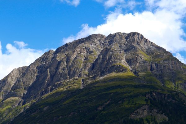 A breathtaking view of a towering rocky mountain peak against a vibrant blue sky with scattered clouds. Nature 4K