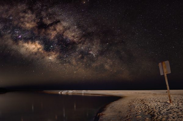 A breathtaking view of the Milky Way galaxy shining brightly over a serene, sandy beach at night. Espace 4K