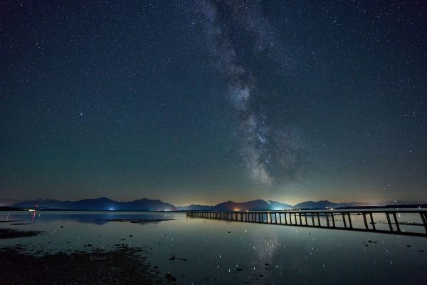 A breathtaking view of the Milky Way reflecting in Chiemsee lake at night, showcasing a tranquil starry night sky. Espace 4K