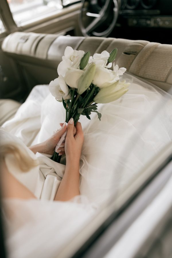 A bride holding a white bouquet sitting inside a vintage car. Perfect for wedding themes. Mobile 4K