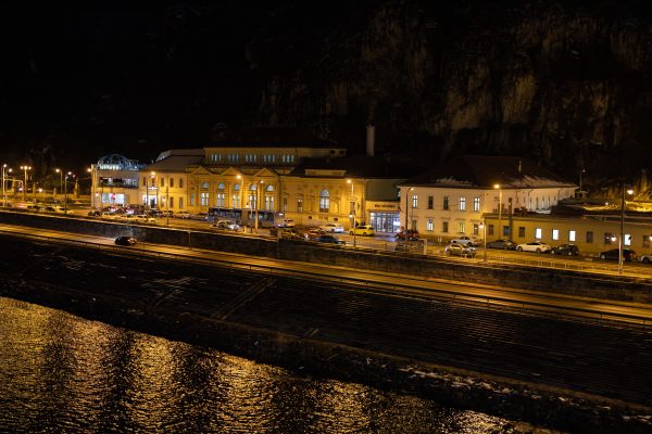 A brightly lit train station by a river at night, reflecting golden lights. Voitures 4K