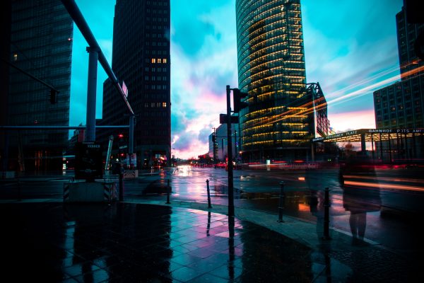 A bustling city street at twilight with modern skyscrapers and vibrant light trails reflecting on wet pavement. Voitures 4K