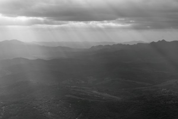 A captivating black and white landscape photo of Minas Gerais with sun rays piercing through clouds. Dark 4K