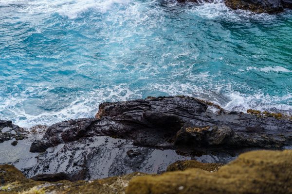A captivating view of rough rocks overlooking the vibrant turquoise ocean waves crashing ashore. Nature 4K