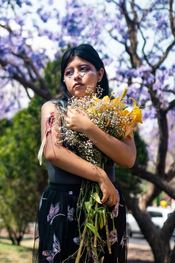 A child in a floral dress holds a bouquet of flowers under jacaranda trees. Mobile 4K