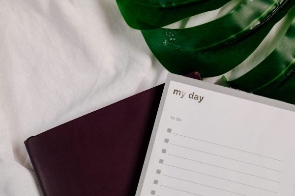 A close-up of a to-do list notebook with lush green leaves on a white textile surface. Minimaliste 4K