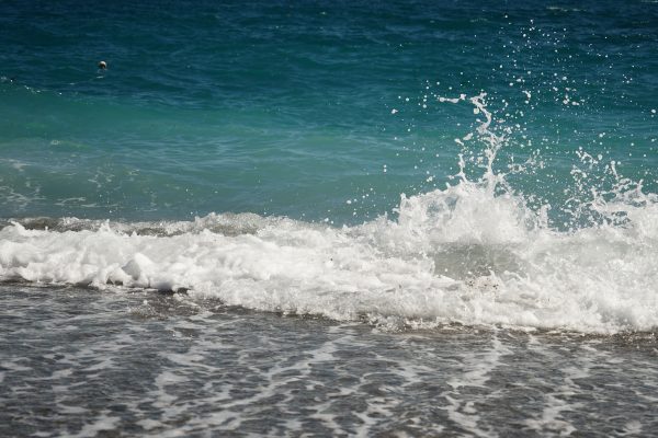 A frothy ocean wave crashes onto a sandy beach under a clear sky, capturing coastal energy. Nature 4K