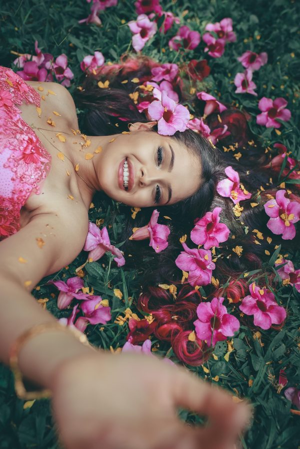 A joyful young woman in a pink dress relaxes among vibrant hibiscus flowers in a lush garden. Mobile 4K