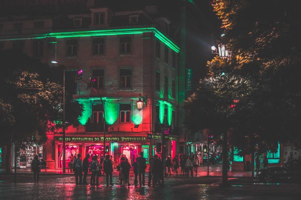 A lively urban street scene at night featuring neon-lit buildings and groups of people. Voitures 4K