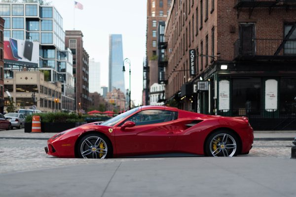 A luxurious red Ferrari sports car parked in urban New York City against a backdrop of modern and vintage buildings. Voitures 4K