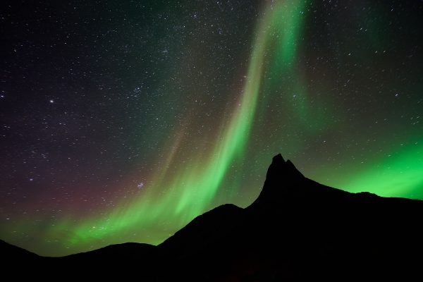 A mesmerizing display of northern lights dancing over a mountainous silhouette and starry night sky. Espace 4K