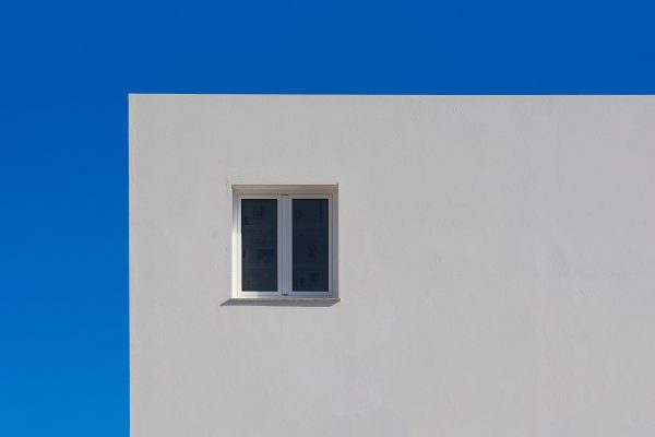 A minimalist image of a white wall with a small window against a vibrant blue sky. Minimaliste 4K