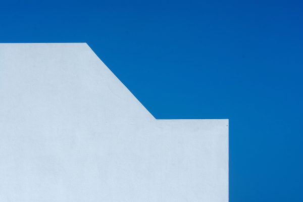 A minimalist photo of a white wall contrasting with a vibrant blue sky, showing geometric simplicity. Minimaliste 4K