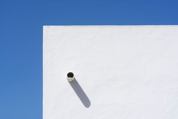 A minimalist white wall casting a distinct shadow under a clear blue sky, showcasing modern architectural design. Minimaliste 4K