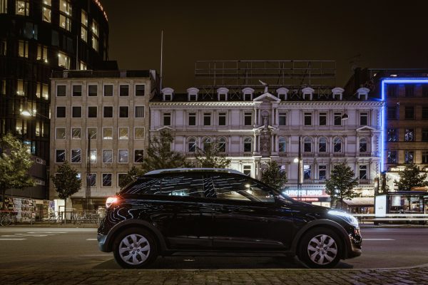 A modern car parked on a city street at night, surrounded by illuminated buildings in an urban downtown area. Voitures 4K