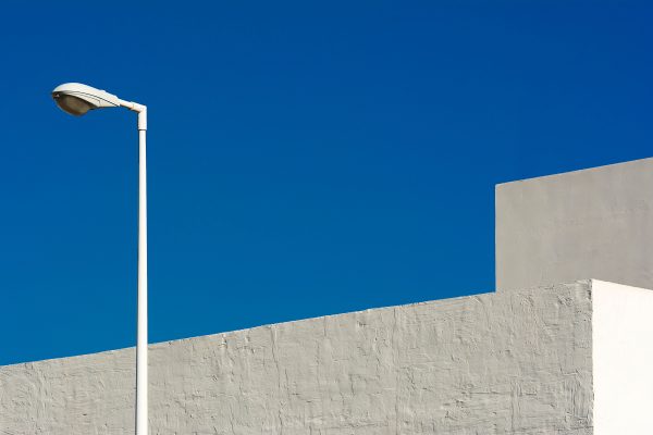 A modern minimalist urban scene featuring a streetlamp against a geometric building and clear blue sky. Minimaliste 4K