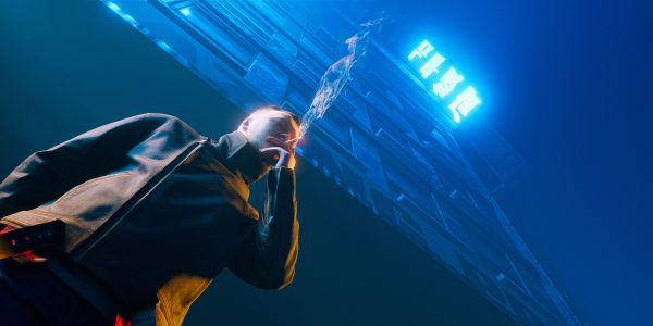 A person smokes under a neon-lit building, creating a moody urban night ambiance. Dark 4K