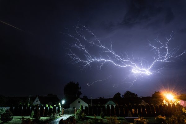 A powerful lightning bolt illuminates the night sky above a suburban neighborhood during a thunderstorm. Dark 4K