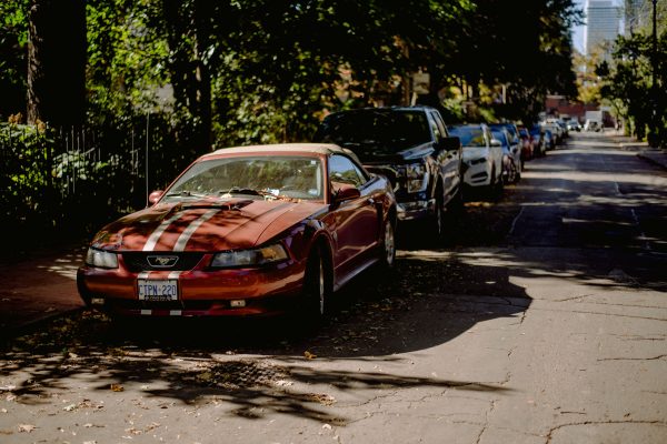 A red Ford Mustang parked along a tree-lined city street on a sunny day. Voitures 4K