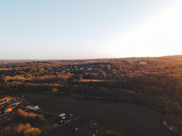 A scenic aerial shot over the English countryside at sunset showcasing houses and a vast forest. Nature 4K
