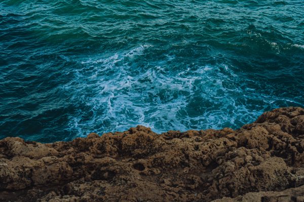 A scenic view of turquoise ocean waves crashing against a rocky shoreline in summer. Nature 4K
