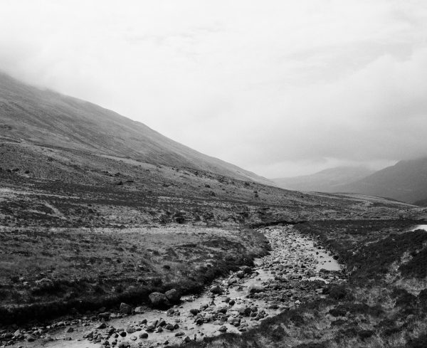 A serene black and white landscape of a stream flowing through the highlands, surrounded by rolling hills. Nature 4K
