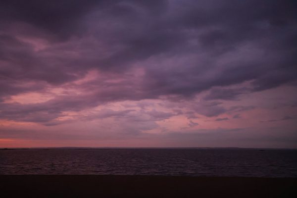 A serene coastal sunset with pink and purple hues reflecting on the calm sea under dramatic clouds. Nature 4K