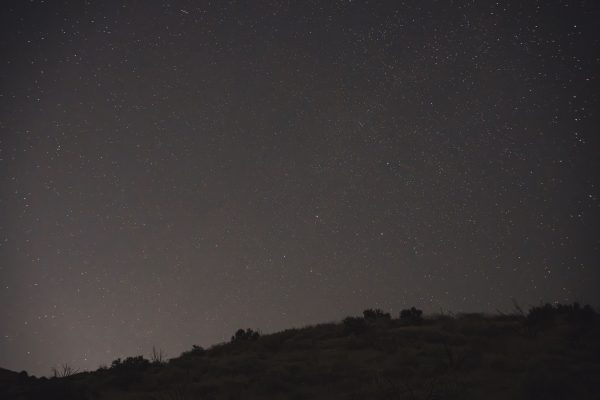 A serene night sky filled with stars above a dark silhouette of a landscape. Espace 4K