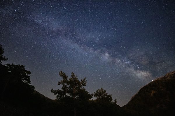 A serene night sky view showcasing the Milky Way galaxy above silhouetted trees in a mountainous landscape. Espace 4K