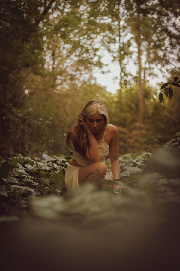 A serene portrait of a blonde woman sitting amidst lush greenery in a tranquil forest during summer. Mobile 4K
