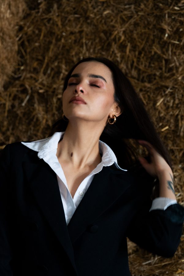 A serene portrait of a woman in a black suit lying on straw. Mobile 4K