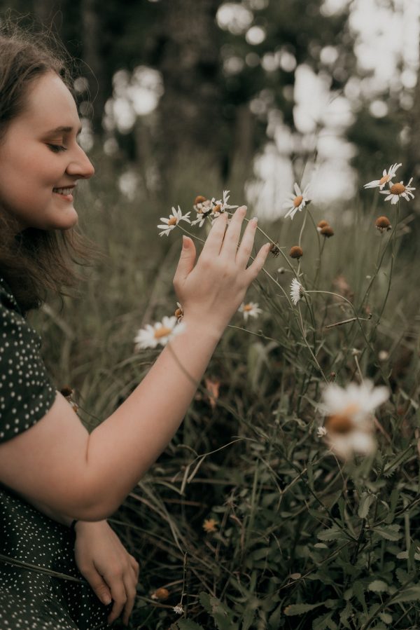 A serene scene of a woman gently touching daisies in a green field, enjoying nature's beauty. Mobile 4K