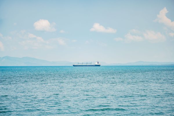 A serene view of a cargo ship sailing on a calm ocean with distant mountains and clear sky. Nature 4K