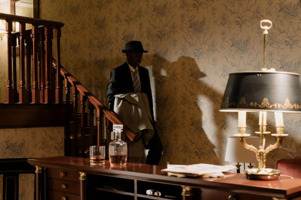 A shadowy detective in vintage attire descends wooden stairs, evoking a classic noir mood. Dark 4K
