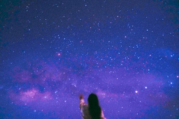 A silhouette of a person reaching towards a vivid starry night sky, featuring the Milky Way. Espace 4K