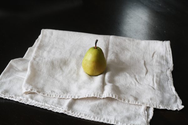 A single fresh pear placed on a white cloth against a dark background, highlighting its natural elegance. Minimaliste 4K