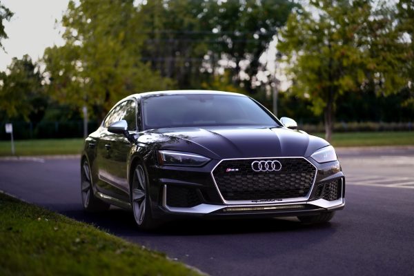 A sleek black Audi RS sedan parked on a tree-lined outdoor road, showcasing modern automotive design. Voitures 4K