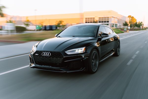 A sleek black Audi RS5 in motion on a city road during daytime. Voitures 4K