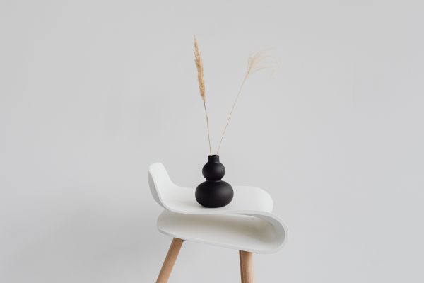 A sleek black vase with wheat ears on a modern white chair against a minimal background. Minimaliste 4K