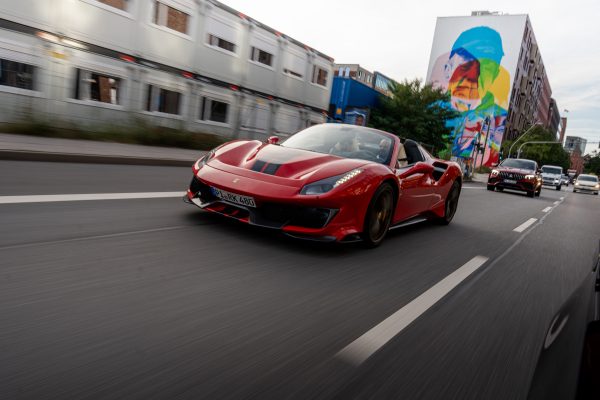 A sleek red Ferrari cruises down a street in Hamburg, Germany, capturing a sense of speed and luxury. Voitures 4K