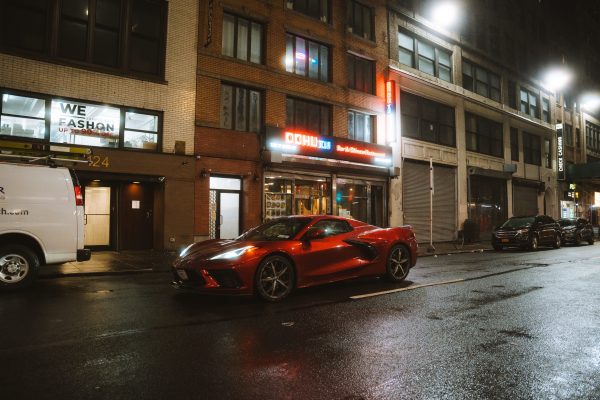A sleek red sports car, possibly a Chevrolet Corvette, parked on a bustling city street at night. Voitures 4K