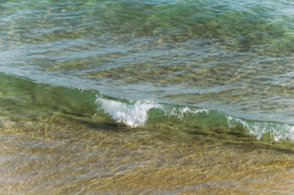 A small wave breaking on the sandy coastline of Ireland, featuring clear turquoise water captured in summer. Nature 4K